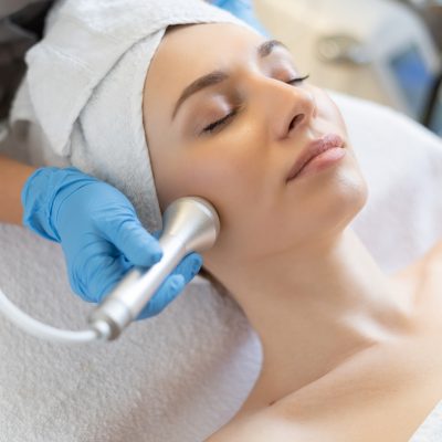 Young woman lying on cosmetologist's table during rejuvenation procedure. Cosmetologist take care about neck and face skin youthfull and wellness. Hardware face cleaning procedure