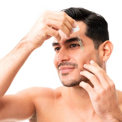 Closeup of a attractive young man in his 20s applying a drop of apply facial serum